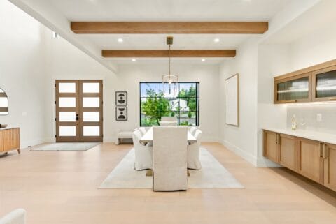 Light and airy dining room scene with a white dinner table and chairs, accented with wood finishing around the room.