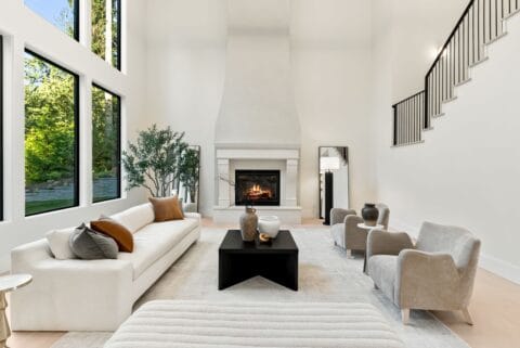 Large, white living room with huge windows and modern furniture with a fireplace in the background.